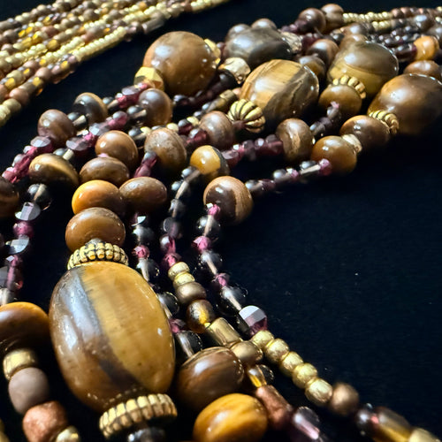 Close-up of multiple beaded necklaces with brown and gold beads on a dark background