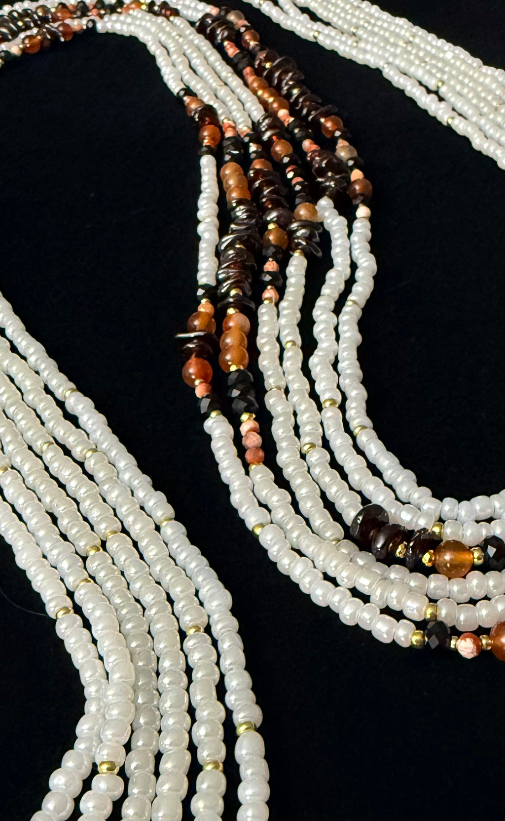 Multiple strands of beaded necklaces with white, brown, and black beads on a black background