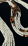 Multiple strands of beaded necklaces with white, brown, and black beads on a black background