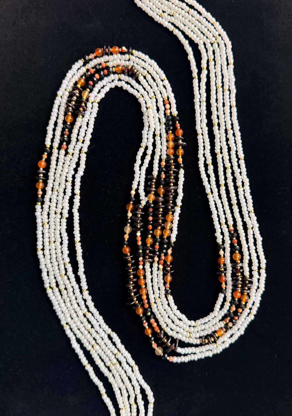 Beaded necklace with white, orange, and black beads on a black background