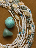 Multiple beaded necklaces with turquoise stones on a brown fabric background