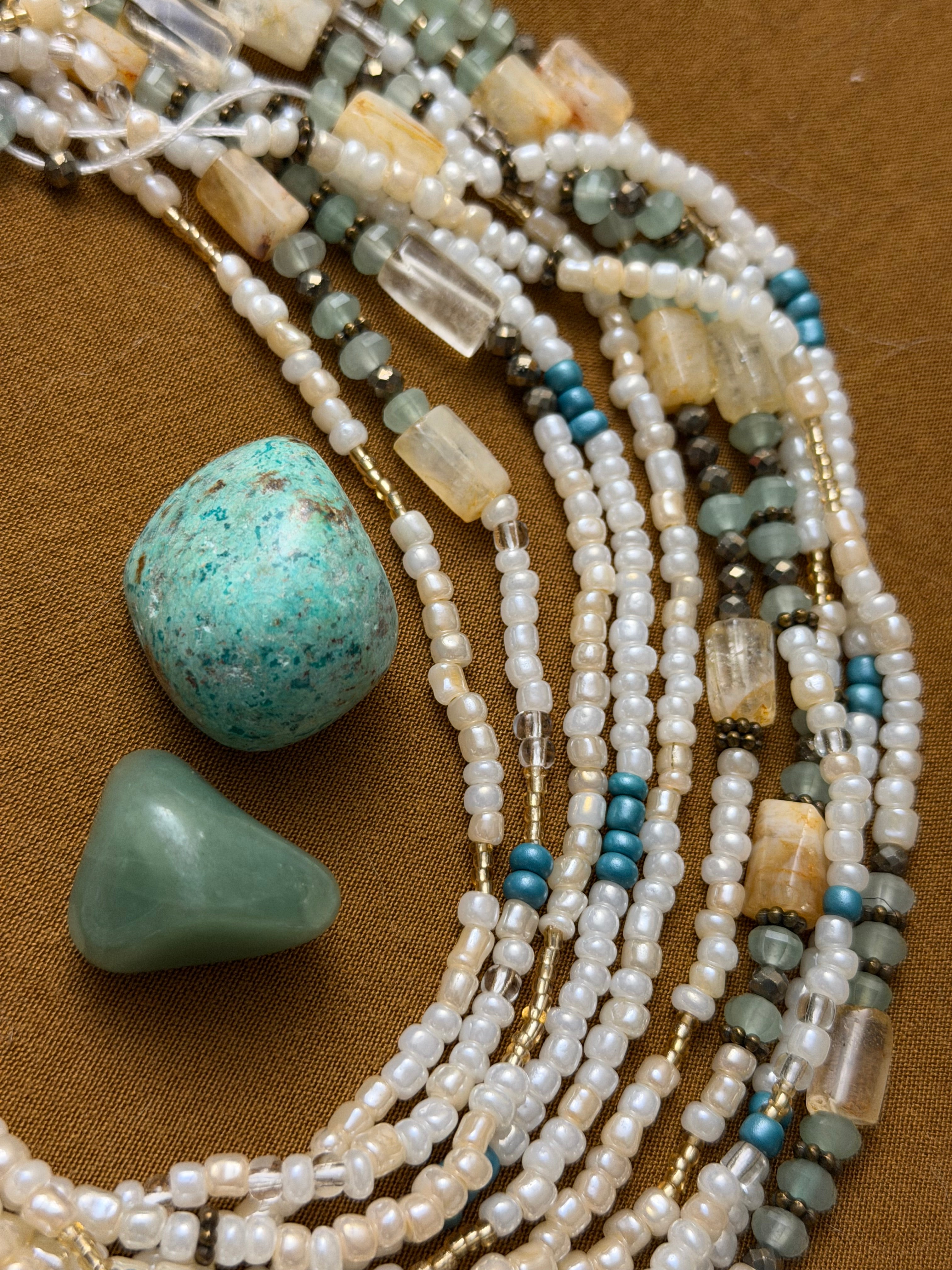 Multiple beaded necklaces with turquoise stones on a brown fabric background