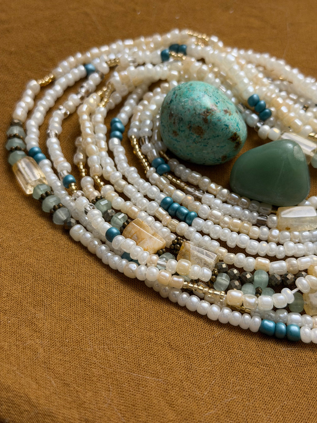 Multiple strands of pearls and turquoise stones on a brown fabric background