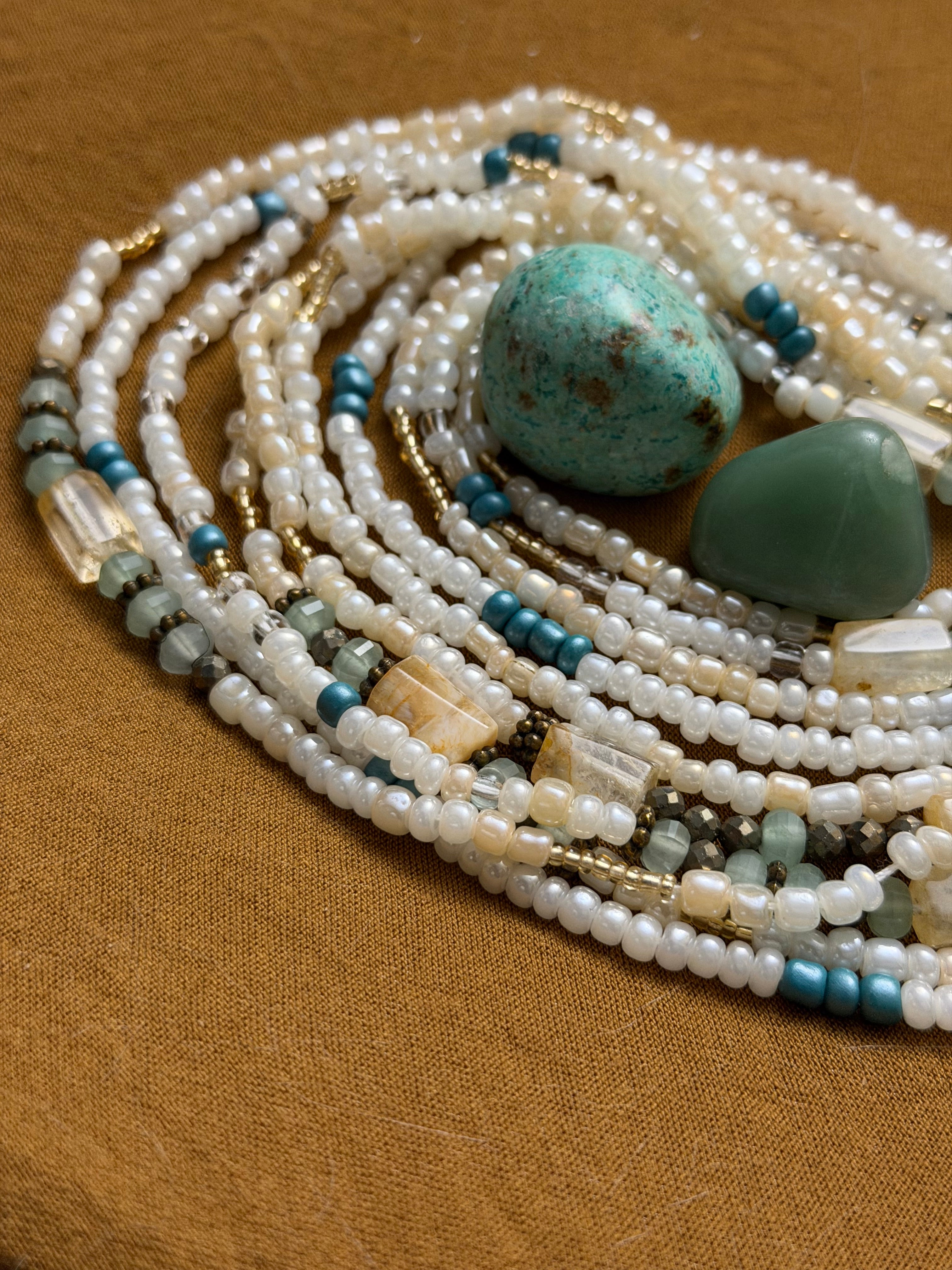Multiple strands of pearls and turquoise stones on a brown fabric background